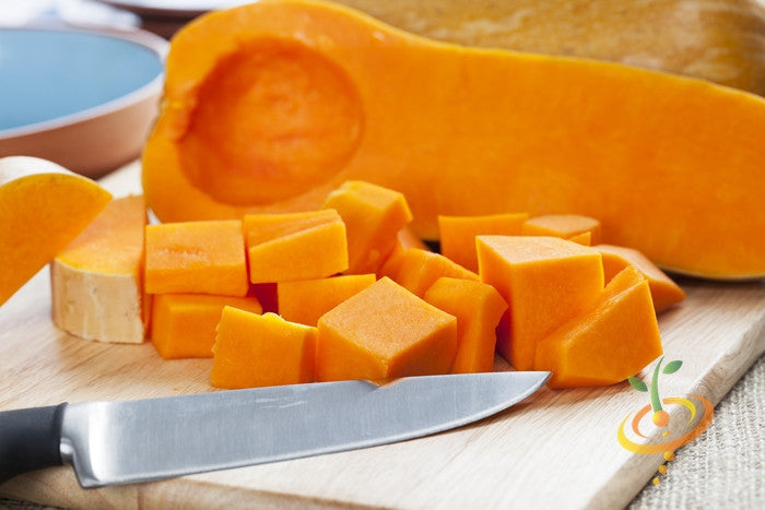Diced Waltham Butternut winter squash with knife on cutting board, showing vibrant orange flesh and smooth tan rind.