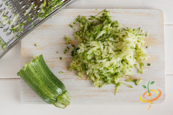 Grated fresh summer squash on cutting board with half a green zucchini and metal grater for summer squash seeds cooking