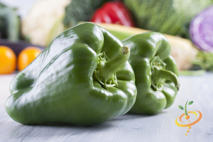 Close-up of two fresh green Ancho Grande hot peppers on a table with blurred vegetables in the background