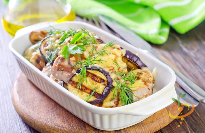 Grilled eggplant aubergine dish with herbs and melted cheese in white baking dish on wooden board