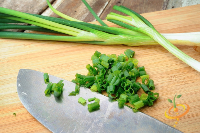 Fresh Tokyo Long White scallions sliced on a wooden cutting board with a knife