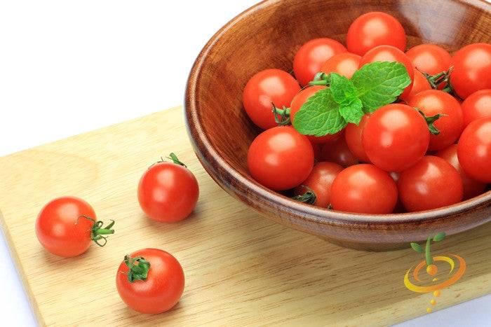 Bowl of bright red Tomato Tiny Tim cherry tomatoes with a few tomatoes on a wooden cutting board and a mint garnish on top